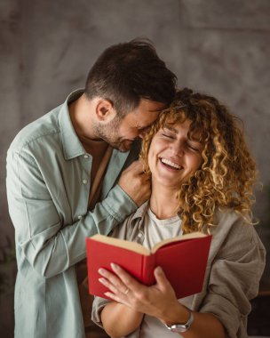 Kız arkadaşı kitap okurken erkek arkadaşı ona sarılıyor.