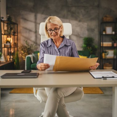 Olgun bir kadın, evden güzel bir mektup zarfıyla açık bir şekilde çalışıyor.