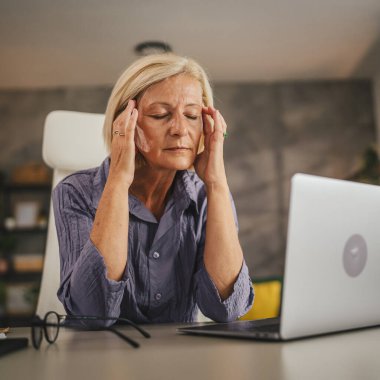 Olgun yaşlı kadın evde çalışıyor ve migren ağrısı çekiyor.