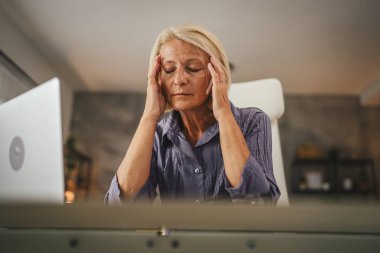 Olgun yaşlı kadın evde çalışıyor ve migren ağrısı çekiyor.