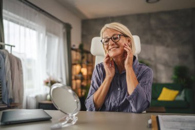 Olgun bir kadın aynada kendine bakar cildini kontrol eder evde çalışırken cildinde lekeler ve kırışıklıklar arar.