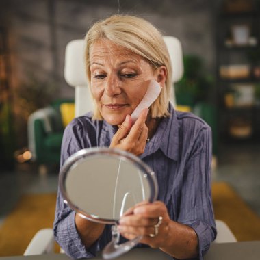 Olgun kadın evinde gül gua sha ile cildine masaj yapıyor.