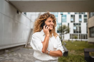 Yetişkin bir kadın binanın önünde cep telefonuyla konuşuyor.