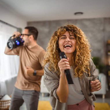 Kız arkadaşı arkada erkek arkadaşıyla mikrofonda karaoke yapıyor.
