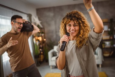 Kız arkadaşı arkada erkek arkadaşıyla mikrofonda karaoke yapıyor.