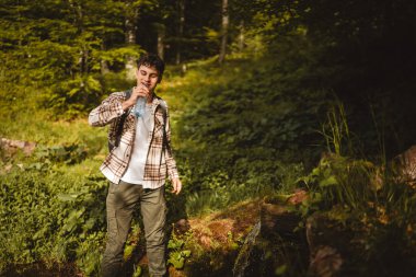 Yetişkin beyaz bir adam ormanda sırt çantasıyla dolaşır.