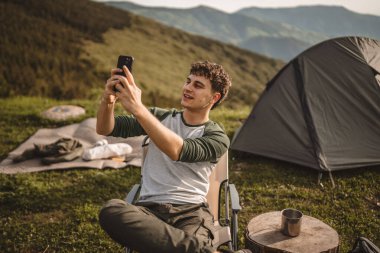 Delikanlı, çadırın önünde otur ve videoya çek ya da dağda kendi portreni yap.