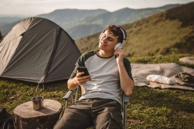 Genç çocuk, sandalyede otur ve kulaklıkla ve cep telefonuyla müzik dinle.