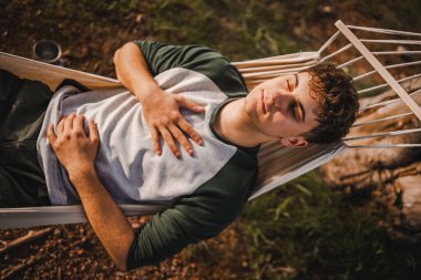 Genç çocuk meditasyon yapıyor ve dağdaki hamakta uzanıyor.