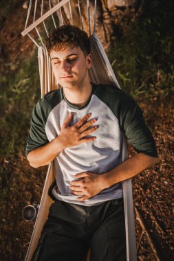 Genç çocuk meditasyon yapıyor ve dağdaki hamakta uzanıyor.