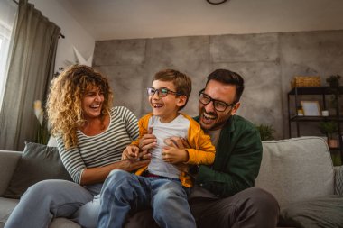 Üç kişilik mutlu bir aile evde eğleniyor. Oğlunu gıdıklıyor ve sarılıyor.