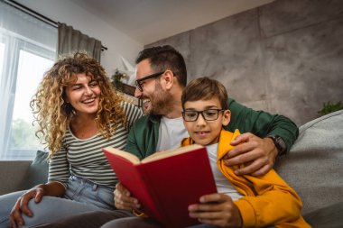 Okumayı öğrenen, kanepede oturan ve evde kitap okuyan oğullarının gururlu ebeveynleri.