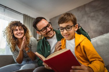 Okumayı öğrenen, kanepede oturan ve evde kitap okuyan oğullarının gururlu ebeveynleri.