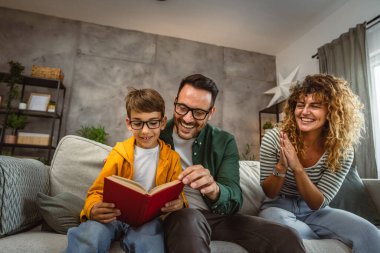 Okumayı öğrenen, kanepede oturan ve evde kitap okuyan oğullarının gururlu ebeveynleri.