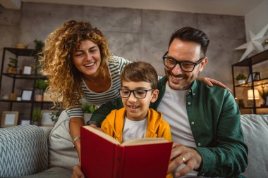 Okumayı öğrenen, kanepede oturan ve evde kitap okuyan oğullarının gururlu ebeveynleri.