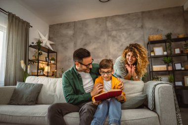 Okumayı öğrenen, kanepede oturan ve evde kitap okuyan oğullarının gururlu ebeveynleri.