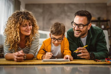 Üç kişilik aile halıya uzanın ve birlikte resim yapın.