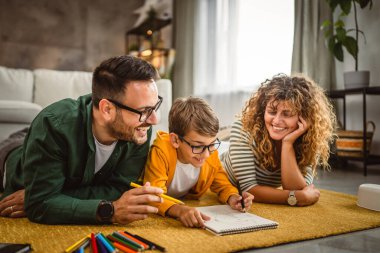 Üç kişilik aile halıya uzanın ve birlikte resim yapın.
