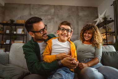 Portrait of mum,dad and son sit on sofa and have family time at home clipart