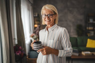 Olgun kadın portresi gülümse ve evde bir fincan kahve tut.