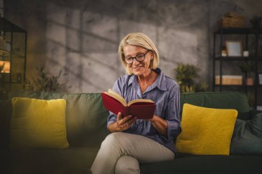 Olgun, son sınıf öğrencisi bir kadın oturma odasında oturup kitap okuyor.