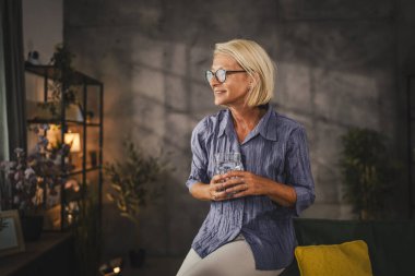 Rahatla olgun kadın portresi otur ve bir bardak su tut.