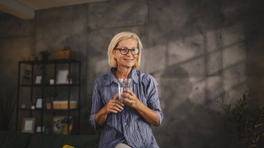 Rahatla olgun kadın portresi otur ve bir bardak su tut.