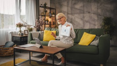 Yetişkin yaşlı kadın evde çalışıyor. Tablet üzerinden video görüşmeleri yapılıyor.