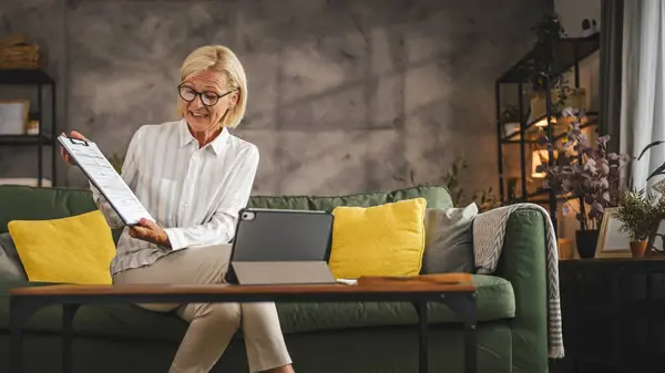 stock image Mature senior woman work from home have consultation via video call on tablet