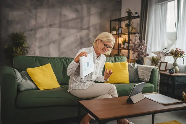 stock image Mature senior woman work from home have consultation via video call on tablet