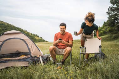 Kamp yaparken kız arkadaşıyla cep telefonu kullanıyor.