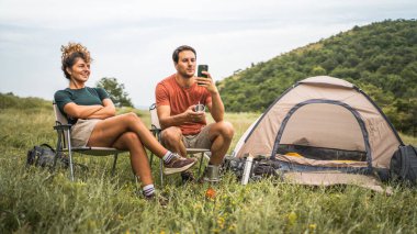 Kamp yaparken kız arkadaşıyla cep telefonu kullanıyor.