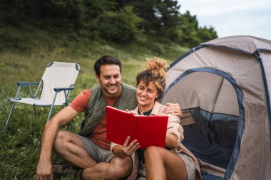 Girlfriend read a book with her boyfriend in front the tent clipart
