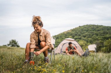 Kız arkadaş arkada erkek arkadaşıyla kamp yaparken kahve hazırlar.