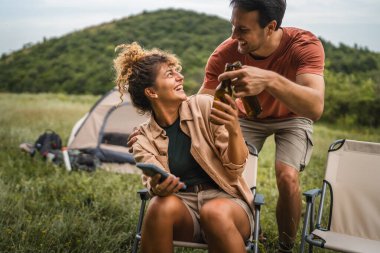 Kız arkadaş cep telefonunu kullanırken erkek arkadaş onlara bira getiriyor.