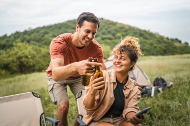 Kız arkadaş cep telefonunu kullanırken erkek arkadaş onlara bira getiriyor.