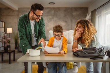 Anne ve baba oğullarına okuldan sonra ödev yapmasına yardım ediyor.