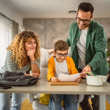 Anne ve baba oğullarına okuldan sonra ödev yapmasına yardım ediyor.