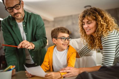 Anne ve baba oğullarına okuldan sonra ödev yapmasına yardım ediyor.