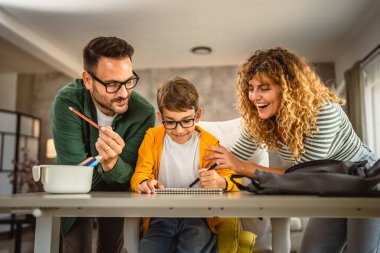 Anne ve baba oğullarına okuldan sonra ödev yapmasına yardım ediyor.