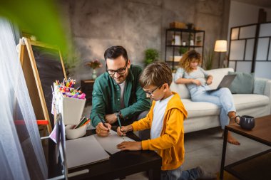 Baba ödevini yap, oğul çiz anne arka planda çalışırken.