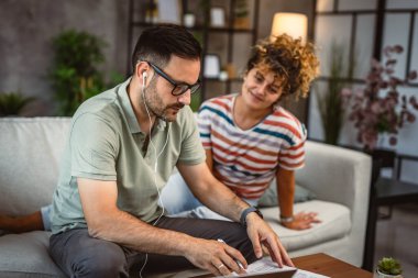 Kulaklık takan adam evde çalışıyor. Kız arkadaşıyla birlikte panoya yazı yazıyor.