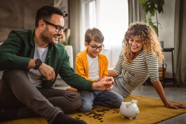 Anne, baba ve oğul halının üzerine oturur ve evdeki kumbarada para biriktirirler.