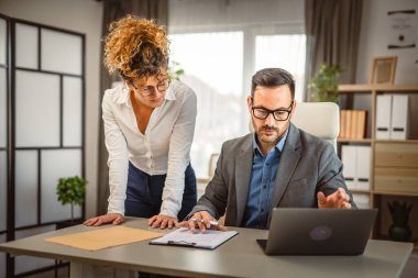 İki meslektaş iş yerinde bilgisayar ve belgeler hakkında istişarede bulunuyorlar.