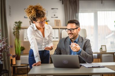 İki meslektaş iş yerinde bilgisayar ve belgeler hakkında istişarede bulunuyorlar.