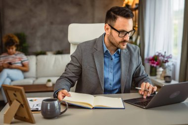 Yetişkin adam arka planda dizüstü bilgisayarla çalışıyor.