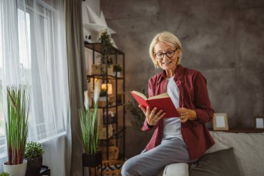 Olgun bir son sınıf öğrencisi. Oturma odasında oturup kitap okuyor.