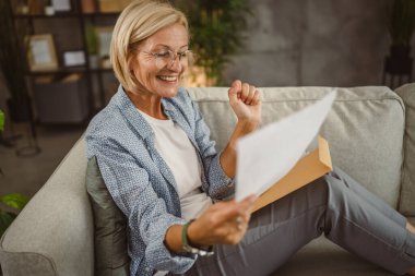 Olgun bir kadın evde çalışıyor. Mektupları iyi haberlerle okuyor.