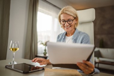 Olgun kadın, pano ve tablet üzerindeki ev analiz belgesinden çalışıyor