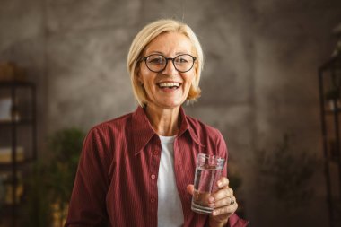 Güzel olgun yaşlı bir kadının portresi otur ve elinde bir bardak su tut.